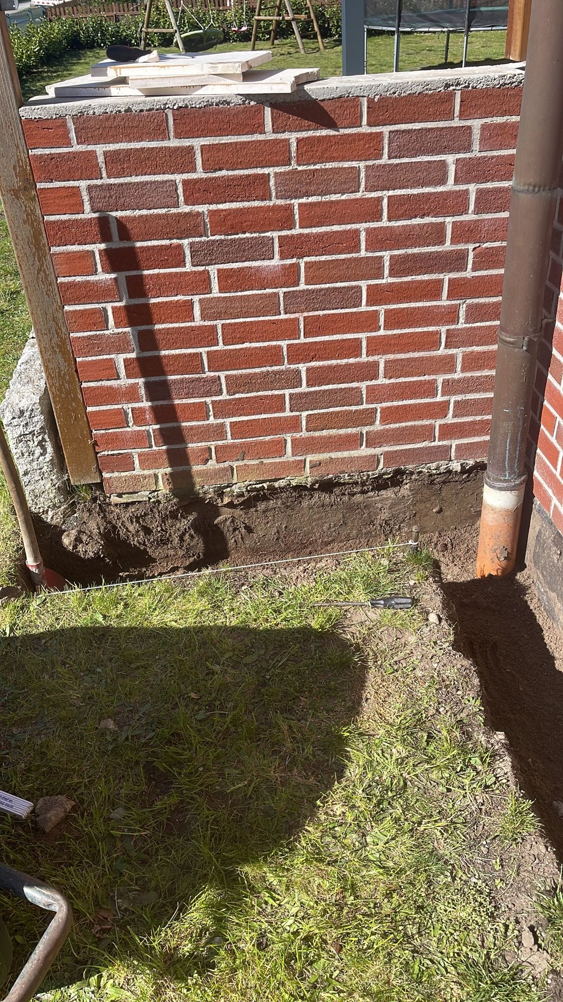 New brick garden wall being built, with the foundation trench still exposed alongside it.