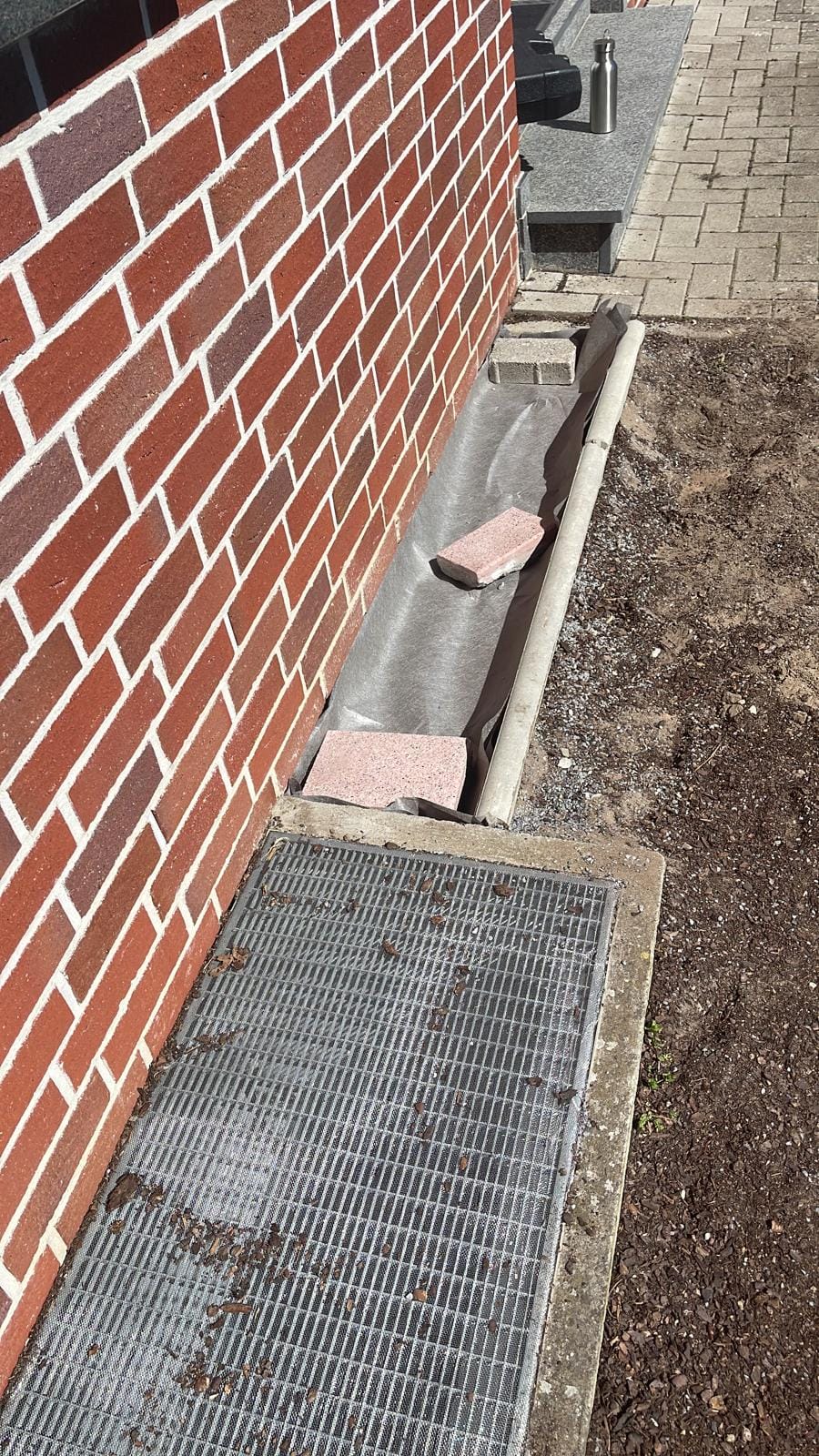 Drainage channel and paving slabs being prepared alongside a brick wall.