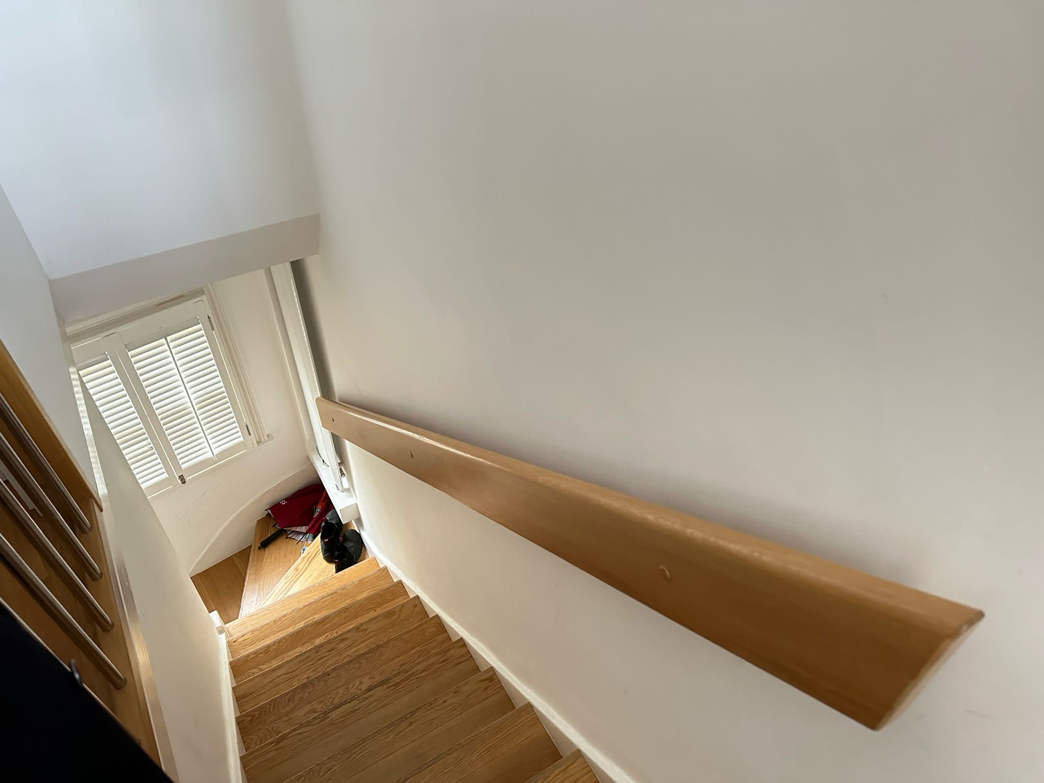 Interior staircase with wooden handrail and plantation shutters.