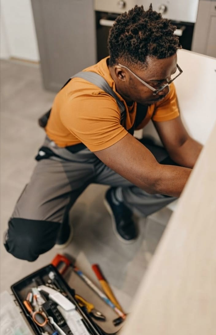 Home maintenance technician repairing a kitchen cabinet using a toolkit.